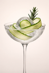 Cucumber tonic cocktail in a coupe glass with cucumber ribbons, ice and a rosemary sprig